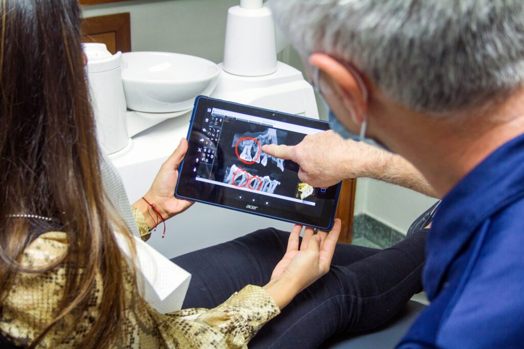 Wisdom Teeth Removal - Over the shoulder image of a dentist pointing to an Xray on a tablet, talking to a patient.